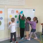 Dzieci rozwiązują zagadkę kropek zawieszonych na tablicy