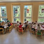 Dzieci w sali przedszkolnej siedzą przy stolikach. Kroją owoce i wkładają do słoików, robią kompoty.