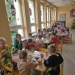 Dzieci siedzą przy stolikach wrzucają owoce do słoików. Dzieci są ubrane w gartuszki.