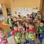 Dzieci ubrane w fartuszki pozują do zdjęcia z wykonanymi przez siebie kompotami.