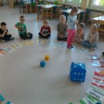Dzieci w kole przy pomocy rozłożonych plansz rozmawiają o swoich emocjach i sytuacjach im towarzyszących