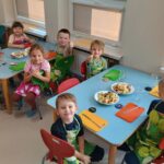 Dzieci uśmiechają się do zdjęcia przy stolikach w fartuszkach