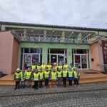 Dzieci w odblaskowych kamizelkach stoją przed Miejskim Domem Kultury.