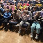 Uśmiechnięte dzieci siedzą w Miejskim Domu Kultury i czekają na przedstawienie "Dziadek do orzechów".