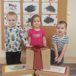 Troje dzieci uśmiecha się, przed nimi stoją zapakowane pudełka ozdobione rysunkami.