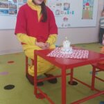 Kubuś Puchatek siedzi przy czerwonym stoliku , na którym jest mały tort z okazji urodzin Kubusia Puchatka.