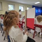Dziewczynka siedzi i trzyma biało- czerwoną flagę.