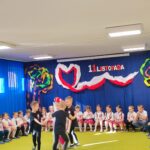Trzech chłopców ubranych na czarno krąży wokół dziewczynki w białej sukience.