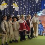Troje chłopców w strojach królów i troje chłopców w strojach pasterzy stoją na scenie z mikrofonem.