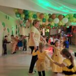 Kobieta tańczy z dziećmi w kole. Wszyscy mają na sobie stroje karnawałowe