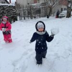 Dziewczynka w kombinezonie rzuca kulką śnieżną.