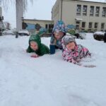 Trzy dziewczynki w kombinezonach leżą na śniegu.