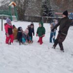 Troje dzieci siedzi na sankach, są ciągnięte przez Pana. Czworo czeka obok na swoją kolej.