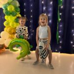 Dziewczynki w strojach karnawałowych pozują do zdjęcia z balonami zebry i krokodyla.