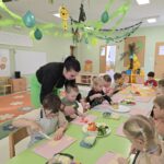 Dzieci w sali przedszkolnej wraz panią krojące warzywa do pizzy na deskach do krojenia