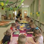 Dzieci w sali przedszkolnej wraz panią krojące warzywa do pizzy na deskach do krojenia