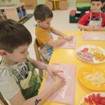 Dzieci w sali przedszkolnej wraz formujące ciasto do pizzy na kształt koła