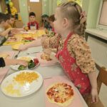 Dzieci w sali przedszkolnej wraz formujące ciasto do pizzy na kształt koła