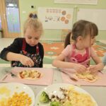 Dzieci w sali przedszkolnej nakładające dodatki na ciasto do pizzy