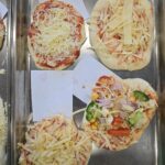 pizze przygotowane przez dzieci na blaszce do pieczenia przed włożeniem do piekarnika