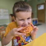 Chłopiec który nagryza własnoręcznie przygotowana pizzę