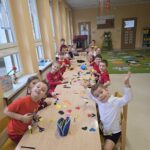 Dzieci przy stolikach wykonują pracę plastyczną z serc.