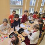 Dzieci siedzą przy stolikach i wykonują pracę plastyczną.
