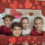 Cztery dziewczynki pozują do zdjęcia trzymając ramkę ozdobioną sercami.