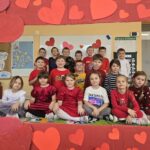 Grupa dzieci pozuje do wspólnego zdjęcia w czerwonej ramce ozdobionej sercami.
