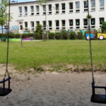 Budynek przedszkola widziany z perspektywy placu zabaw z widokiem na huśtawki