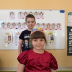 Dziewczynka w czerwonej sukience z papierową koroną oraz uśmiechnięty chłopiec