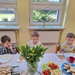 3 chłopaków siedzi przy stole wielkanocnym i jedzą śniadanie.