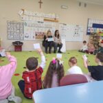 Dzieci siedzą na dywanie i zgłaszają się podczas zajęc.