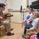 Dziewczynki słuchają dźwięków wydawanych przez gitarę