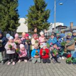 Grupa przedszkolna pozuje do zdjęcia przed budynkiem przedszkola. Każdy w ręce trzyma kwiat.