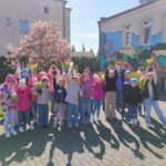 Grupa przedszkolna dzieci pozuje do zdjęcia. Każdy z nich trzyma wysoko w górze kwiat. Wszyscy są zadowoleni.
