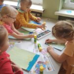 Dzieci wykonujące prace plastyczną przy stoliku