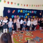 Dzieci ubrane galowo stoją przed napisem Pasowanie na Przedszkolaka.